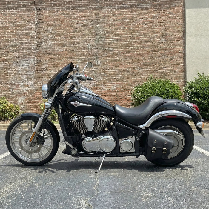 Black Kawasaki Vulcan motorcycle parked in a parking lot with a brick wall background.