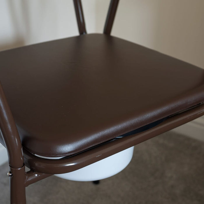 Person emptying or cleaning the commode pan of NRS Dovedale Adjustable Commode with Detachable Arms into a standard toilet.