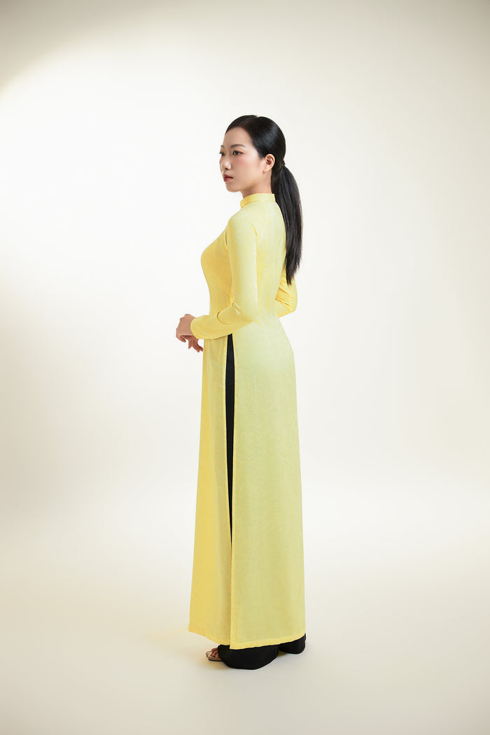 Side view of pale yellow silk brocade Ao Dai showcasing its flowing design.