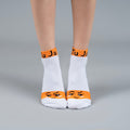 White socks with orange accents and smiley face design on a gray background-Ultimate Roast Socks- Fun Expression-