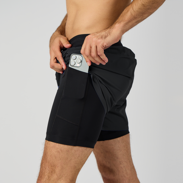 Side view of the Men's Vento™ 4" 2-in-1 Short in the color black, with a hand shown putting a phone in one of the phone-sized compression pockets.