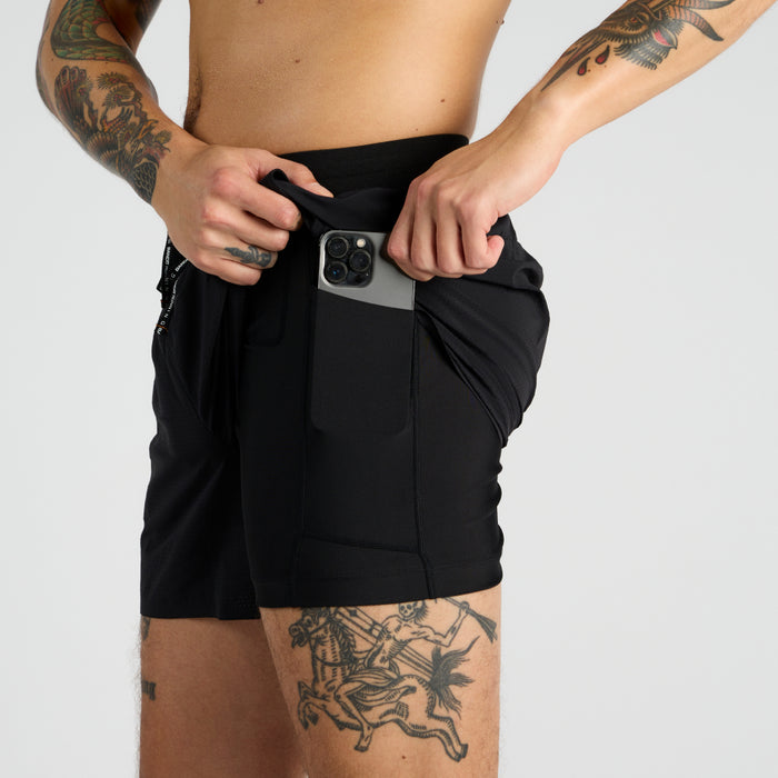 Side view of the Vento™ 5" Men's Training Short, featuring a custom waistband and branded drawsting with a hand shown putting a phone into one of the internal phone-sized compression pockets.